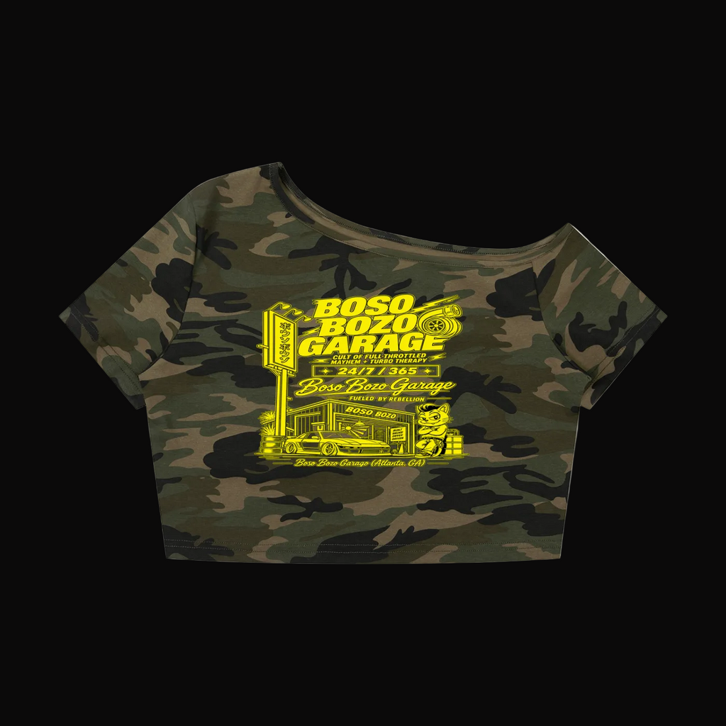 A women's off-the-shoulder crop top featuring a green and black camouflage pattern with a bright yellow graphic print on the front that reads 'BOSO BOZO GARAGE' and depicts a garage scene.